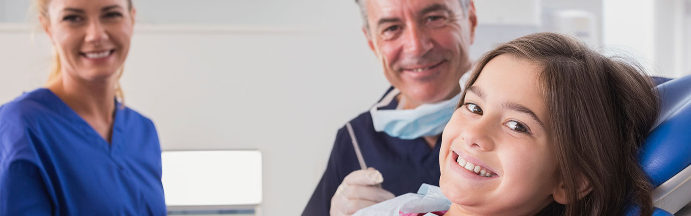 Girl smiling in dentist chair with dentist sitting behind her.